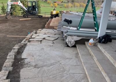 A patio under construction with flagstone paving and a scenic backdrop of a lush landscape with construction materials and equipment visible.