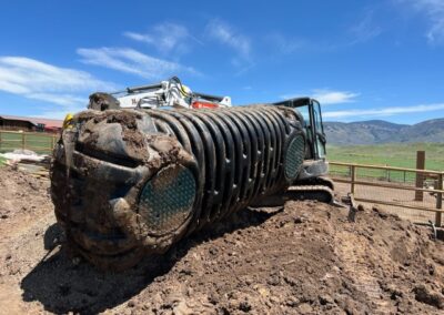 A large industrial vehicle with tank treads toppled over on its side at a construction or agricultural site, surrounded by a dirt terrain and a clear blue sky.