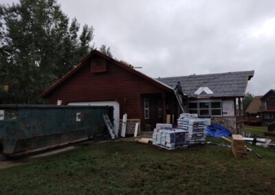 Home renovation in progress with materials and a dumpster on site under an overcast sky.