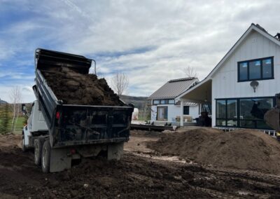 A dump truck unloading soil at a residential construction site with modern houses in the background.