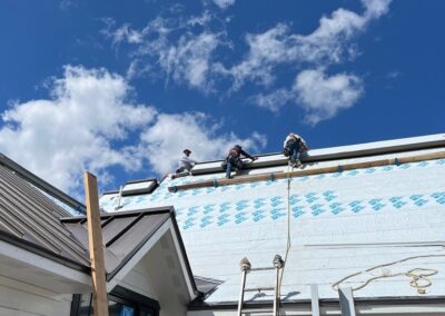Workers on a rooftop under a clear blue sky, installing or repairing a house roof.